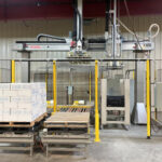 Gantry robot system in a cold storage facility, with pallets of boxed products being prepared for palletizing and freezing, surrounded by safety fencing and automation controls.